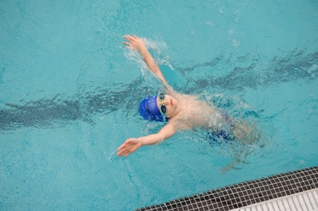 top view of a 7-year boy swimming backstroke in a swimming pool