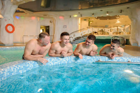close up photo of 4 men relaxing on the top of a swimming pool in a spa centreの写真素材