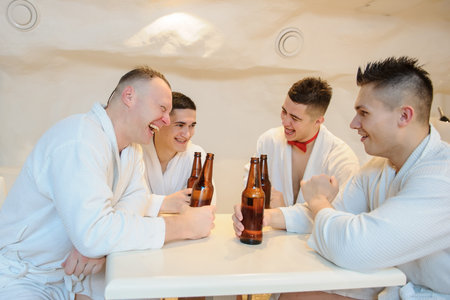 close up photo of 4 men in white gowns sitting around a table and drinking beer after sauna proceduresの写真素材