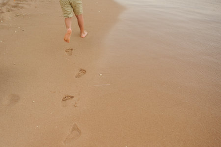 little boy walking on the beach and leaving footprints in the sandの写真素材