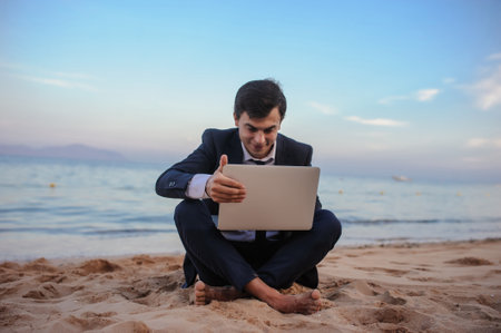 close up photo of a young man in suit with laptop working on the beach and talking to someoneの写真素材