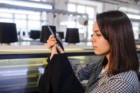 lateral view of a young woman analyzing a knitted piece of cloths near industrial knitting machine with black cones on itの写真素材