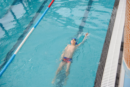 top view of a 7-year boy swimming backstroke in a swimming poolの写真素材