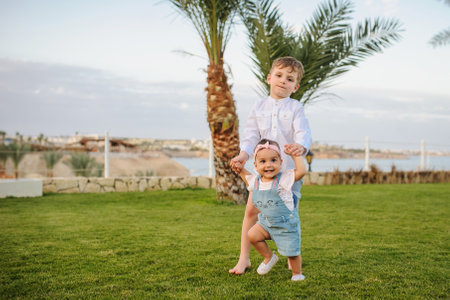 close up photo of a 7-year blond boy walking with his little sister in the garden of a resort in a tropical destinationの写真素材