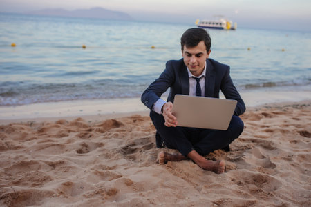 close up photo of a young man in suit with laptop working on the beach and talking to someoneの写真素材