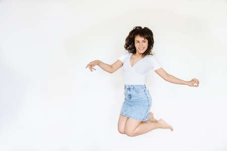 close up photo of a happy brunette in white blouse and denim skirt jumping in the airの写真素材