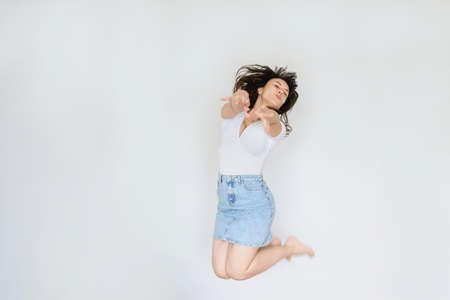close up photo of a happy brunette in white blouse and denim skirt jumping in the airの写真素材