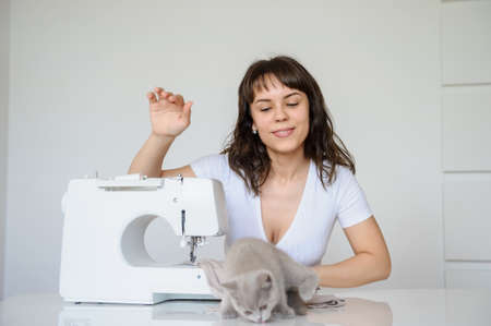 close up photo of a sexy brunette working at the sewing machine and playing with a gray kittenの写真素材