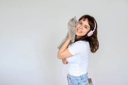 close up photo of a happy brunette with pink headphones listening to the music while holding a gray kitten in her armsの写真素材
