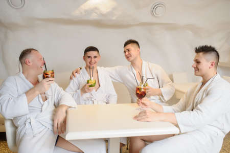 close up photo of 4 men in white gowns sitting around a table and drinking sangria and limonadeの写真素材