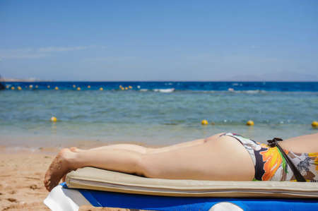 lateral view of a sexy young woman laying on the lounger on the beachの写真素材
