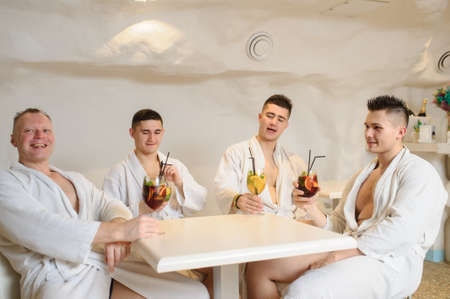 close up photo of 4 men in white gowns sitting around a table and drinking sangria and limonadeの写真素材