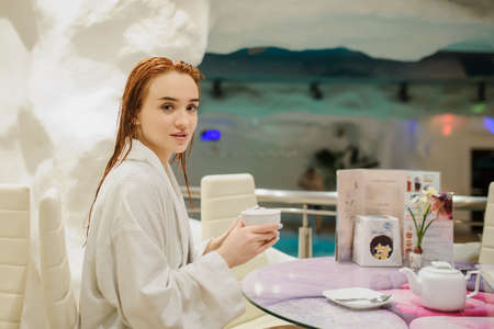 close up photo of a sexy beautiful reddish woman in white bath gown drinking tea in the fito bar of a spa centreの写真素材
