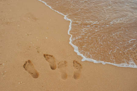 Footprints of human feet on the sand near the water on the beachの写真素材