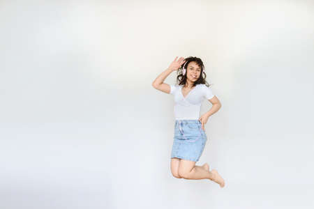 close up photo of a happy brunette with pink headphones in white blouse and denim skirt jumping in the airの写真素材