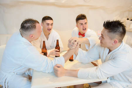 close up photo of 4 men in white gowns sitting around a table and drinking beer after sauna proceduresの写真素材