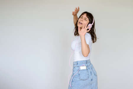 close up photo of a happy brunette with pink headphones in white blouse and denim skirtの写真素材