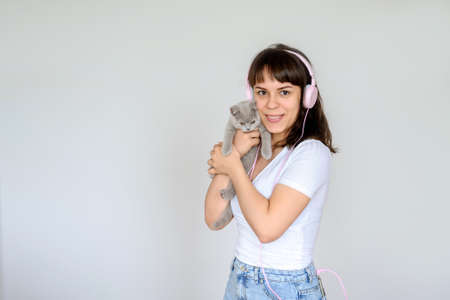close up photo of a happy brunette with pink headphones listening to the music while holding a gray kitten in her armsの写真素材