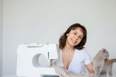 close up photo of a sexy brunette working at the sewing machine and playing with a gray kittenの写真素材