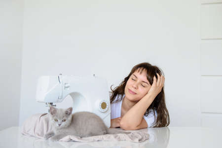 close up photo of a sexy brunette working at the sewing machine and playing with a gray kittenの写真素材