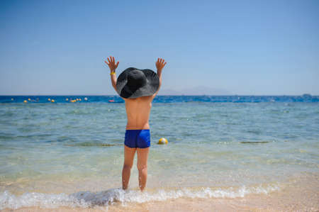back view photo of a 7-year boy on the beach looking at the seaの写真素材