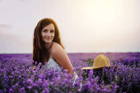 Portrait of a young woman in white dress and straw hat walking in the lavender field. Lavender flowers in bloom.の写真素材