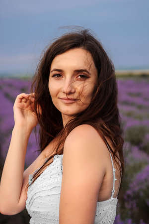 Portrait of a young woman in white dress  walking in the lavender field. Lavender flowers in bloom.の写真素材
