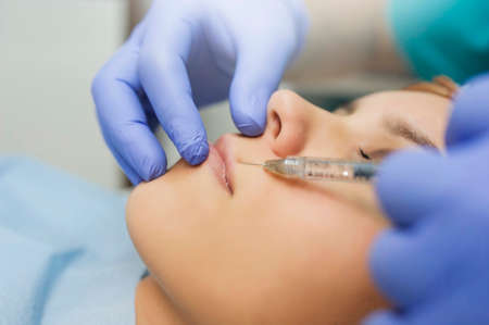 Close up cosmetologist hands in gloves introducing Hyaluronic acid in patient lips with perfect skin. Big lips. Lip augmentation procedure.の写真素材