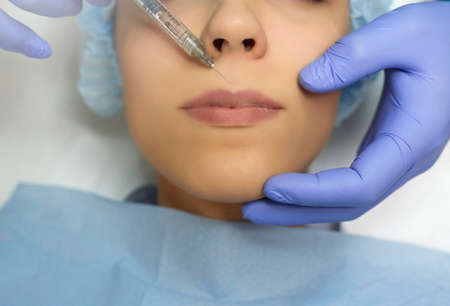 Close up cosmetologist hands in gloves introducing Hyaluronic acid in patient lips with perfect skin. Big lips. Lip augmentation procedure.の写真素材