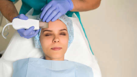 Close up cosmetologist hands in gloves making ultrasound cleaning procedure to the patient's face with perfect skin. Anti Aging procedure.の写真素材