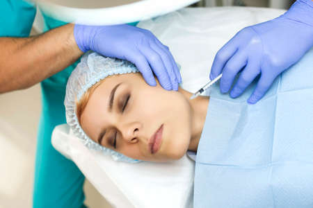 Close up cosmetologist hands in gloves introducing botulinum toxin in the patient's face with perfect skin. Antiaged procedure.の写真素材