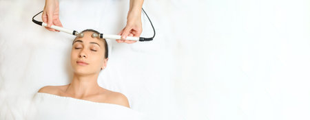 Top view of middle aged woman receiving electrical stimulation facial skin care spa procedure....