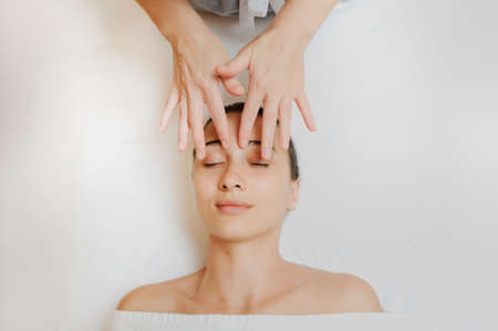 Top view of Woman having curative facial massage. Therapist applying pressure with fingers on forehead. Massage with handsの写真素材
