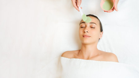 Close up of a woman having a green mask applied. Therapist applying the mask on the skin and...