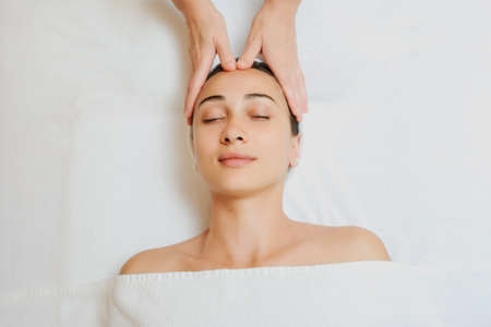 Top view of Woman having curative facial massage. Therapist applying pressure with fingers on forehead. Massage with handsの写真素材