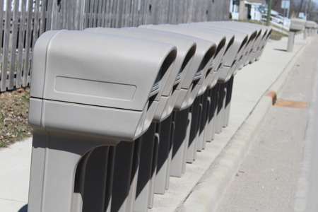 Several Identical plastic mailboxes in a row at the edge of a streetの写真素材