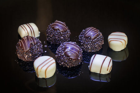 Luxurious chocolate and vanilla pralines truffles, decorated in purple light. Pralines designed in Belgium and arranged on the table. Chocolate candies on a dark background.の写真素材