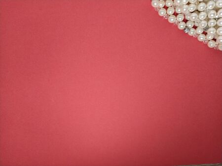 A sheet of paper is red. At the top right, a fragment of a bracelet made of light pearls. Lighting in the center. Background or postcard. Free space for text. Women's jewelryの写真素材