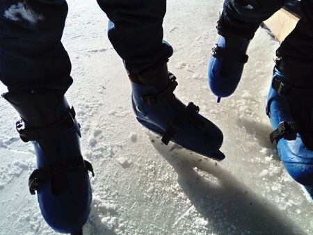 Feet with skates. Sports uniforms and equipment. Ice rink. Long shadows on ice from the low winter sunの写真素材