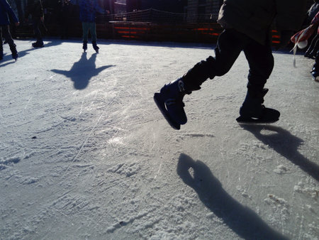 Children ride in a city park on an ice rink. Feet skater while skating on ice. The low winter sun...