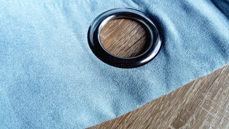 Metal grommet on a gray-blue velvet curtain. The fabric lies on a wooden table. The hole on the...