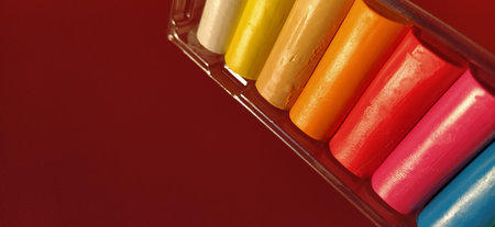 Multi-colored new plasticine in plastic packaging on a red background. Plasticine plates of red,...