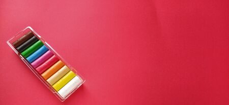 Multi-colored new plasticine in plastic packaging on a red background. Plasticine plates of red, pink, green, white, yellow, brown, blue, black. Set for children's creativity.の写真素材