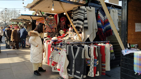 A woman of Asian appearance looks at goods in a street shop. On the window of the stall are beautiful knitted sweaters, vests, coats. Souvenir fair.のeditorial素材