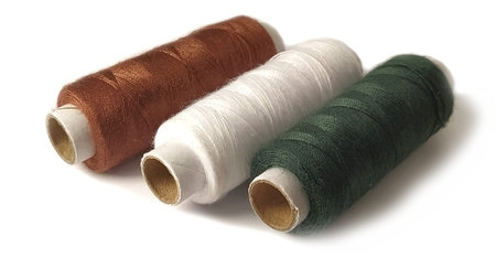Bobbins and spools of thread of different colors - brown, white and green. Close-up. Natural light...