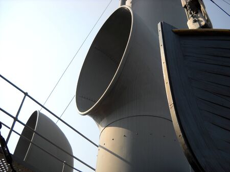 Large bent metal exhaust ship pipes against the blue sky. The metal bottom of a dark wooden lifeboat. Metal cables, fence and equipment. Sea romance. The theme of freedom. Industry, metal casting.の写真素材