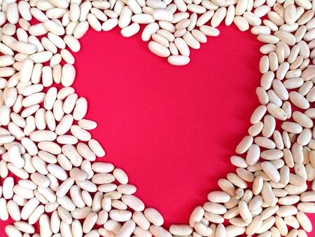A heart shape surrounded by white beans. Bean grains lie beautifully on a red background. Expression of feelings and love. Greeting card Happy Valentine's Dayの写真素材