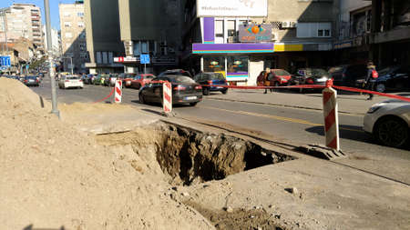Belgrade, Serbia - January 24, 2020. A dug hole in the street of Balkans in Belgrade. Men at work. Destroyed asphalt. A fenced-off site for laying or repairing underground pipes. City Infrastructureのeditorial素材
