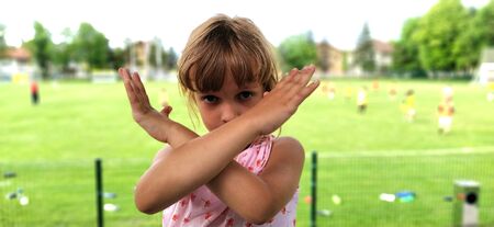 Beautiful girl with brown hair shows hand gestures. Crossing of hands, signifying the end, prohibition, no, stop. In the background is a soccer field. Game over.の写真素材