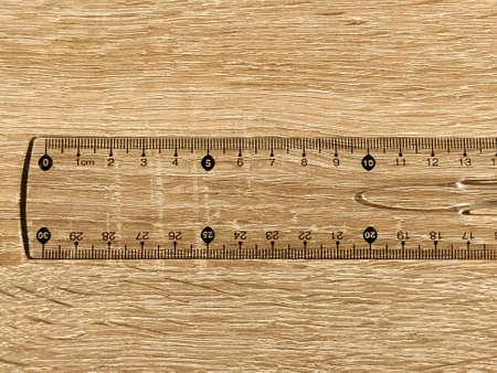 Transparent plastic school ruler on a wooden table. Millimeters and centimeters are marked in black. Measuring length and width with a ruler.の写真素材